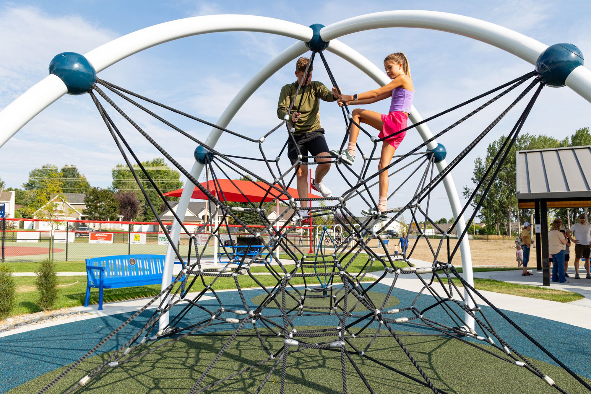Kids climb a rope structure at an outdoor playground under clear, sunny skies.