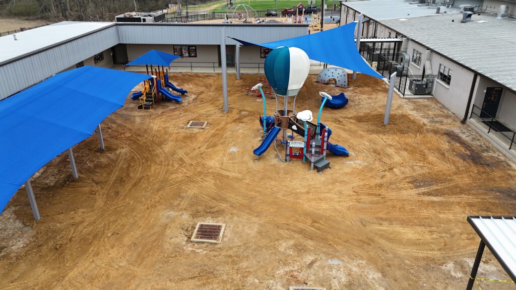 School courtyard playground with blue canopies, slides, and a hot air balloon-themed play structure.
