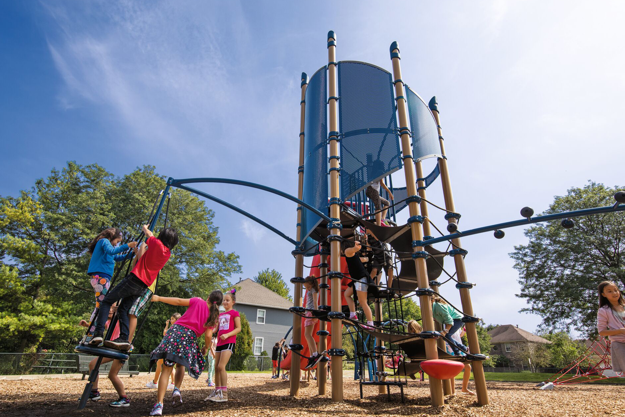 Kids climb and play on a big modern playground structure outside beneath a bright, sunny sky.
