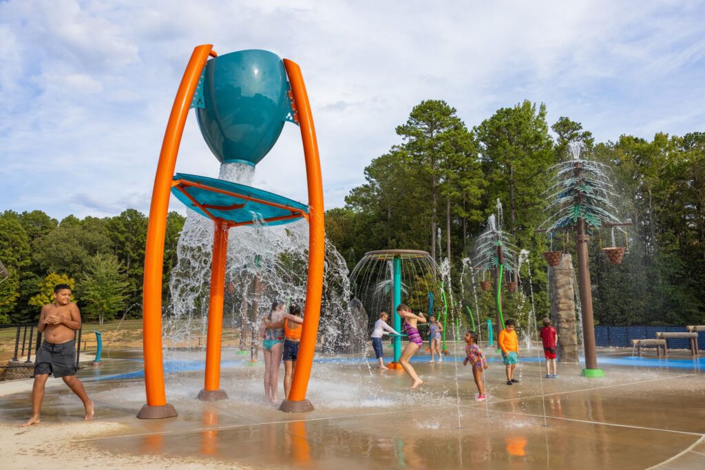 Kids play as a giant bucket spills water over a vibrant splash pad under bright sun.