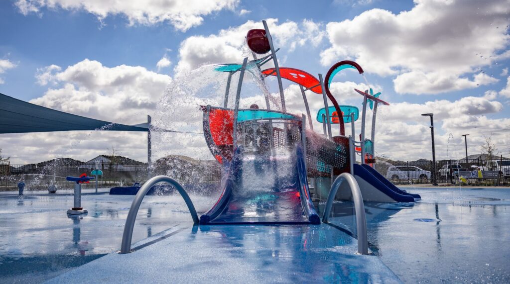 Bright water playground with slides, sprayers, and splashing water beneath a partly cloudy sky.