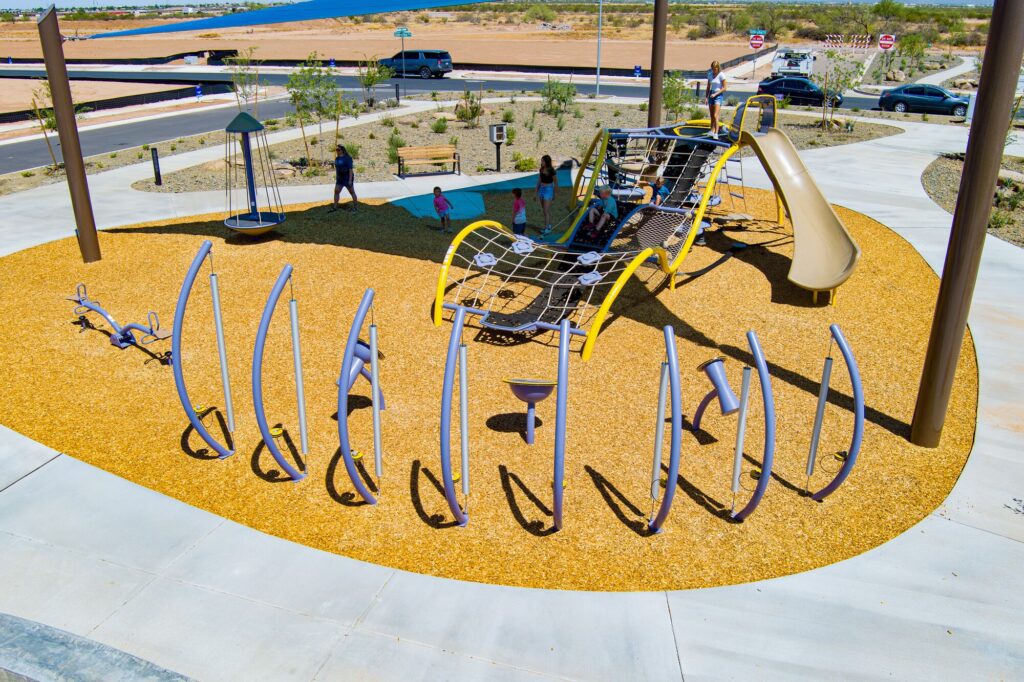 Kids enjoy a modern playground with climbing frames and slides beneath a shade canopy in a leafy park setting.