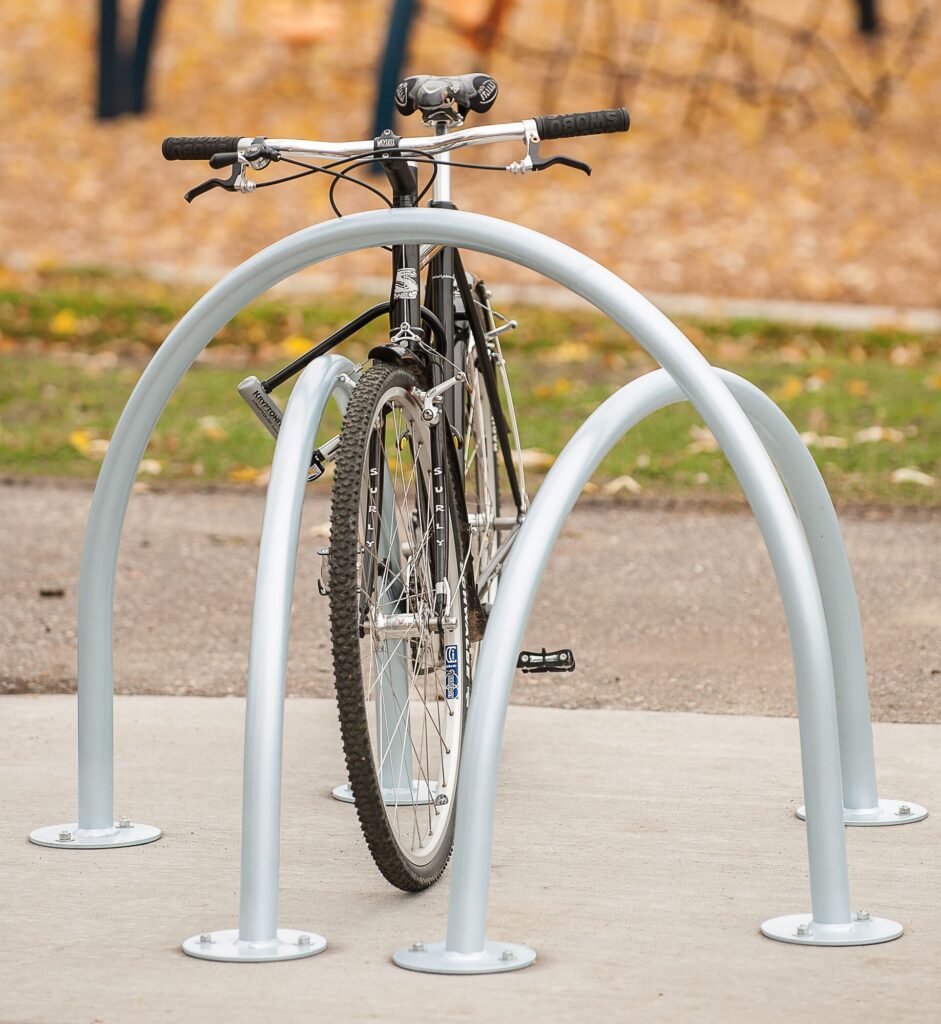 Black bicycle locked to a sleek silver rack outdoors on concrete.