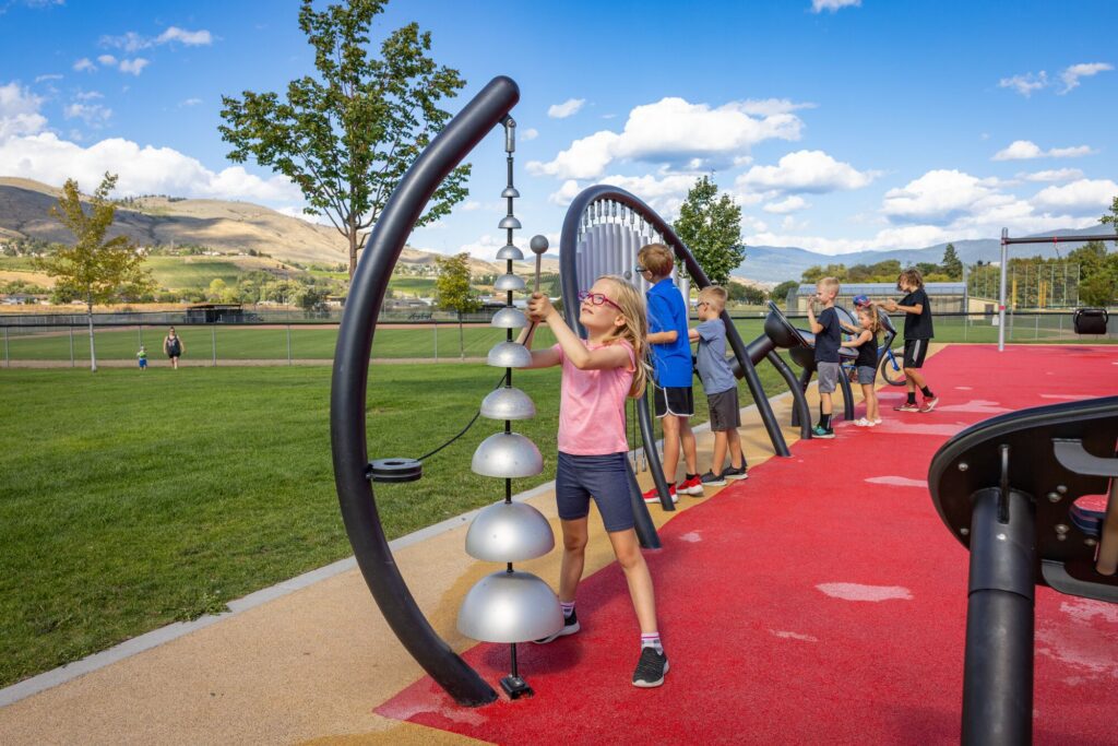 Kids play with musical instruments and equipment on a playground set against a backdrop of mountains.