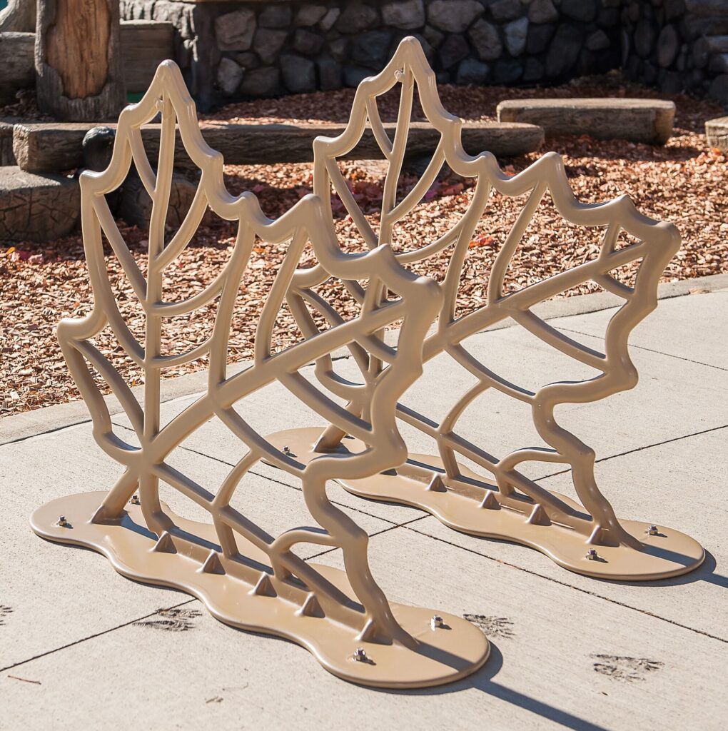 Tan leaf-shaped metal bike racks on concrete, near scattered rocks and wood chips.
