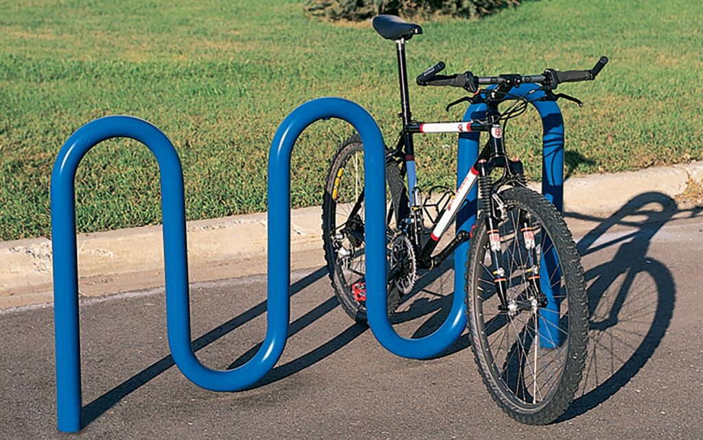Black bike locked to a blue wavy rack on a paved area, with green grass visible nearby.