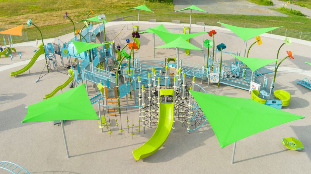 Playground featuring green canopies, slides, climbing nets, and bright flower decorations.