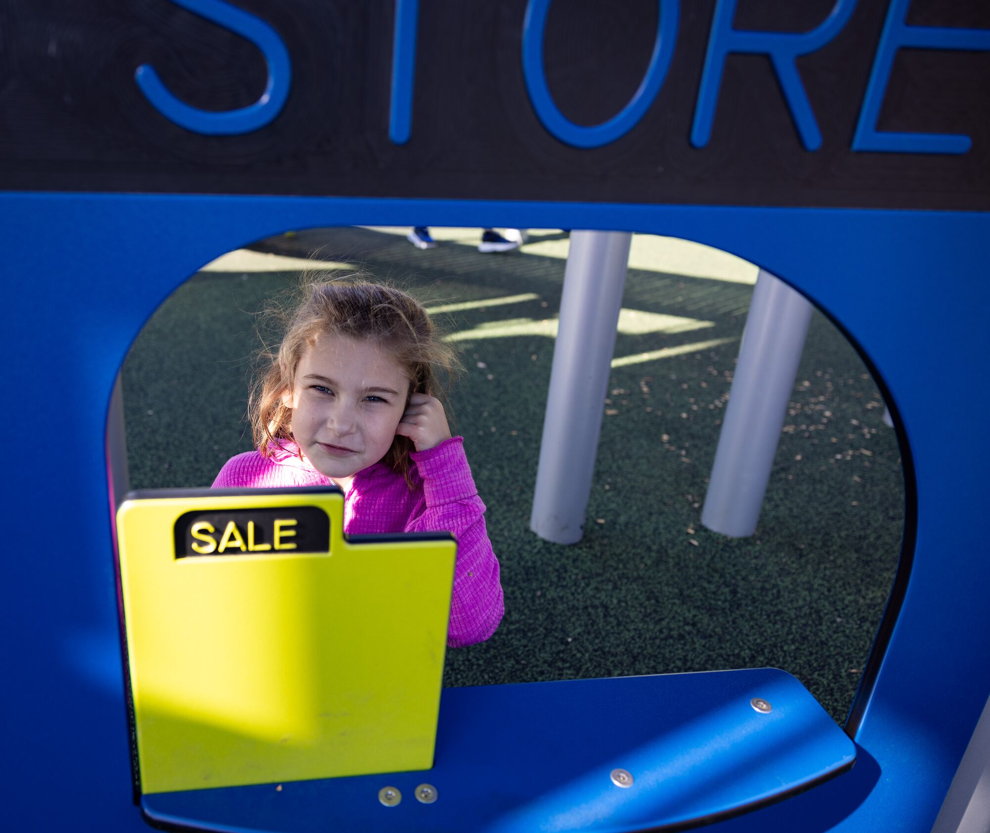 Girl in a pink sweater stands at a playground play store, behind a yellow SALE sign.
