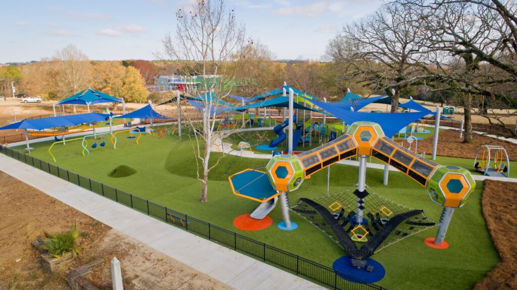 Modern playground with bright climbing frames, slides, swings, and sunshades on green artificial turf.