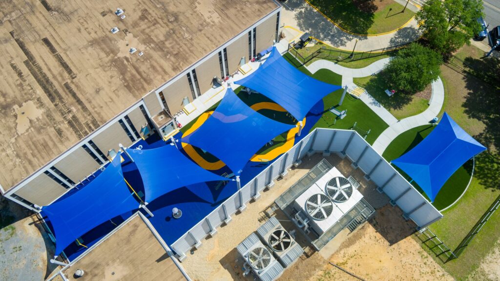 Aerial view of a building with blue shade sails covering a playground and surrounding outdoor space.