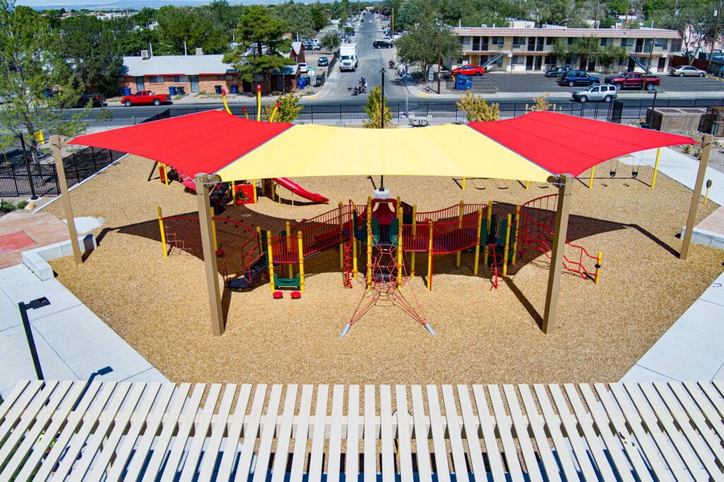 Playground seen from above with red and yellow shade sails covering climbing structures and slides.