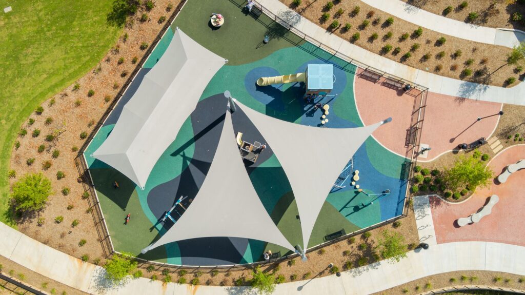 Aerial view of a playground with shade sails, slides, and bright play areas surrounded by landscaped paths.