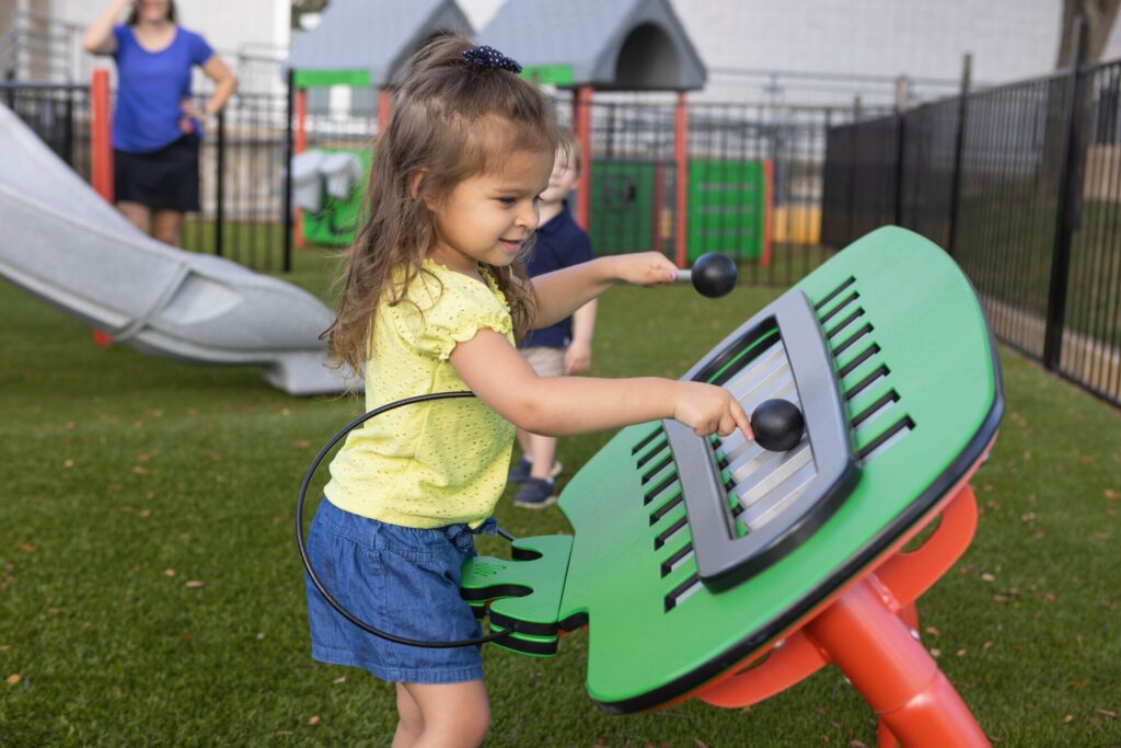 Smiling young girl at playground turns black knobs on a green interactive panel.