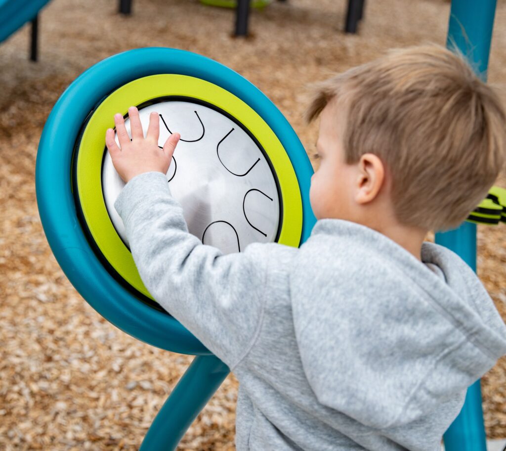 Young boy reaches out to touch a round playground activity panel, engaging with the play equipment.