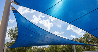 Blue shade sails span between poles beneath a partly cloudy sky, with trees visible in the background.